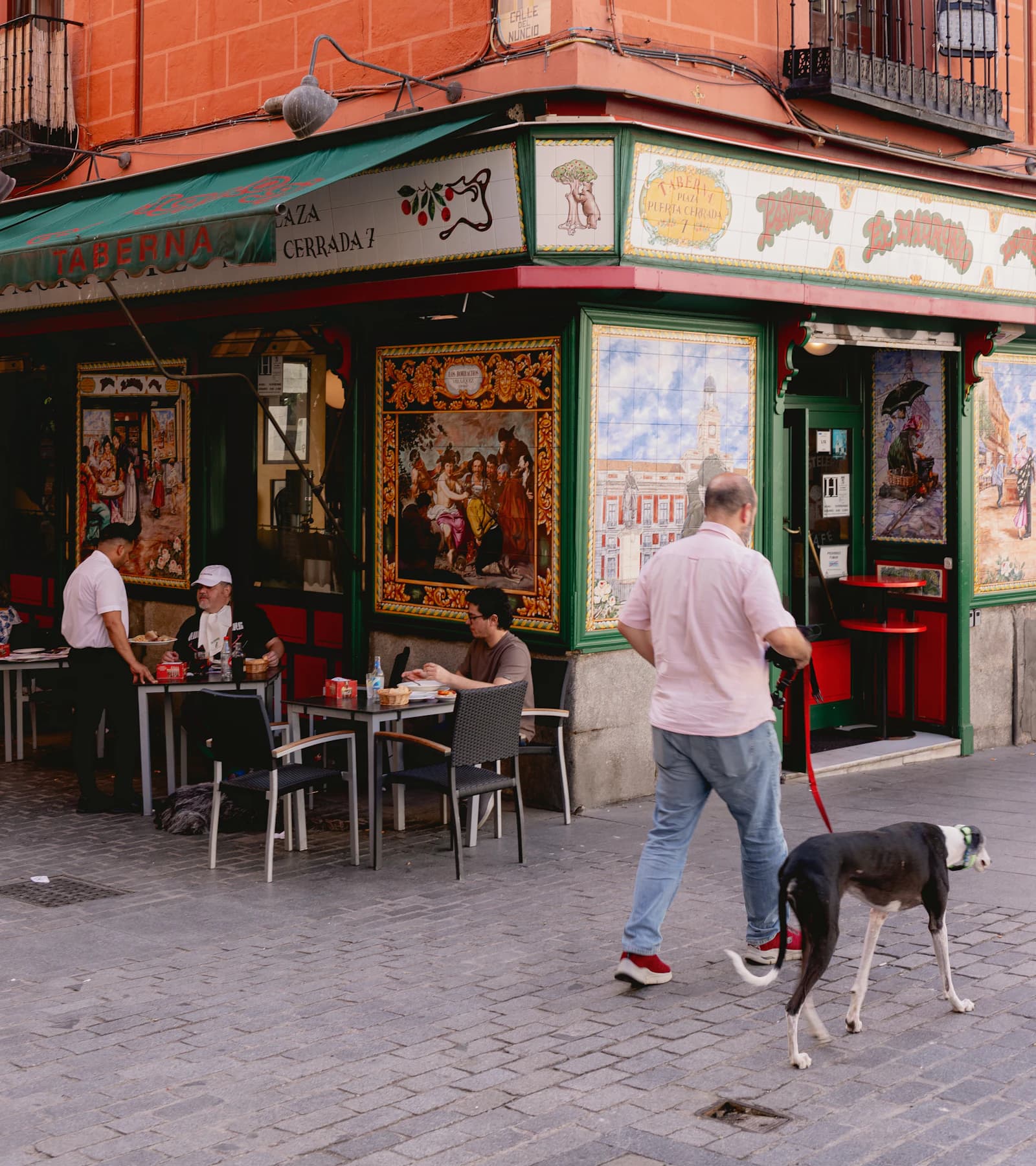 A person walking their dog past a traditional Madrid restaurant